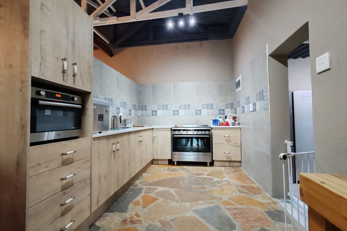 Modern farmhouse kitchen featuring light wood cabinetry, built-in oven and microwave, stone tile flooring, and exposed roof trusses.