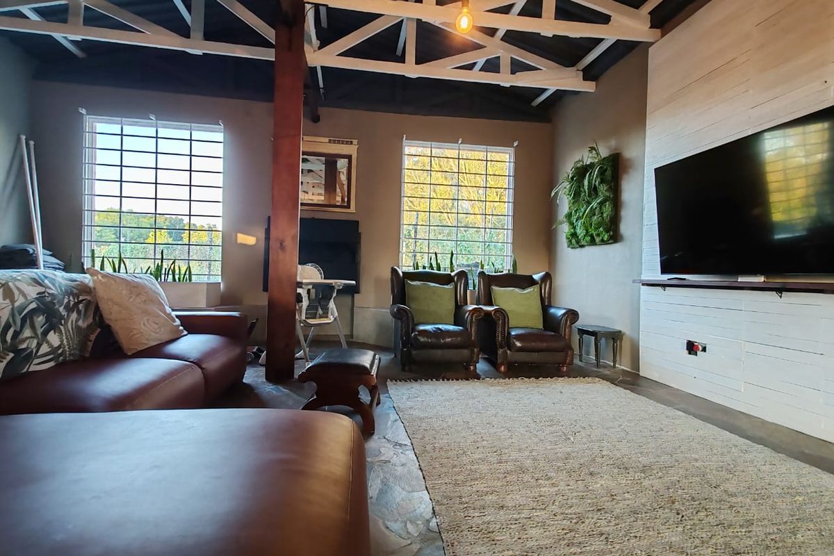 Spacious living room featuring exposed roof trusses, stone flooring, and a feature wall, offering a rustic farm-style aesthetic with ample natural light.