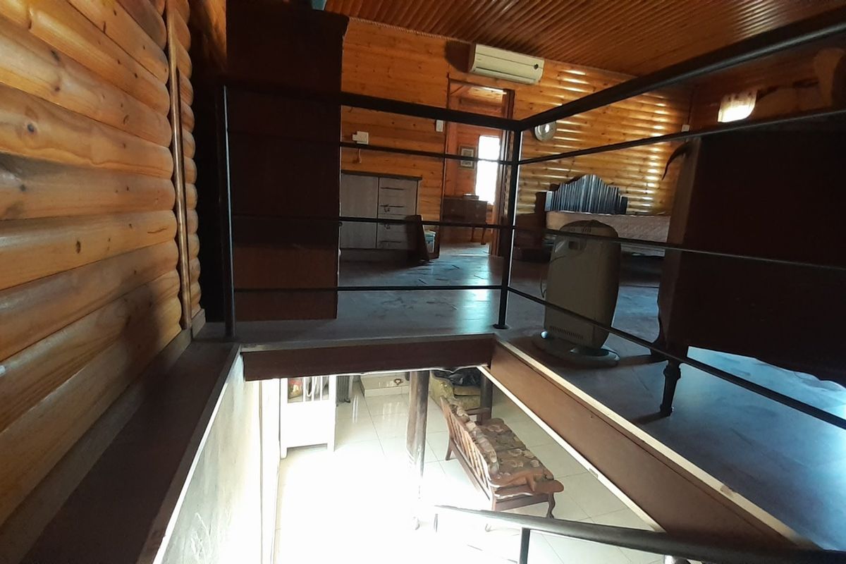 A loft-style bedroom featuring log cabin walls, timber ceiling, and a metal balustrade overlooking the lower level.