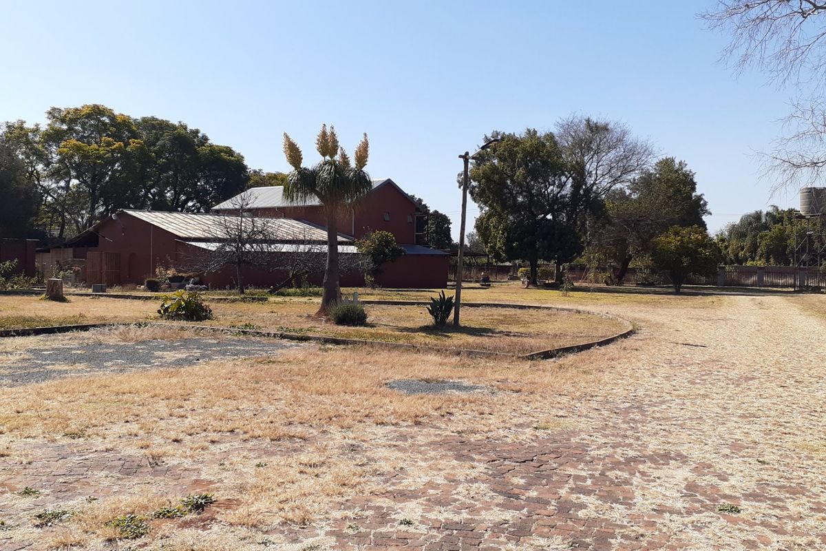 A wide view of the farm property grounds featuring a brick paved driveway, mature trees, and a water tank tower in a rural setting.