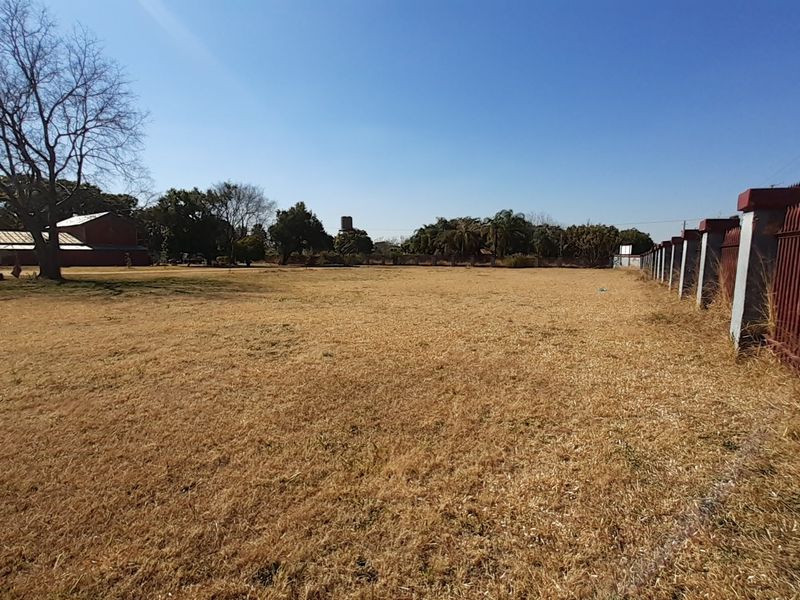 Expansive open field on a farm property featuring perimeter fencing with masonry pillars and mature trees in the background.