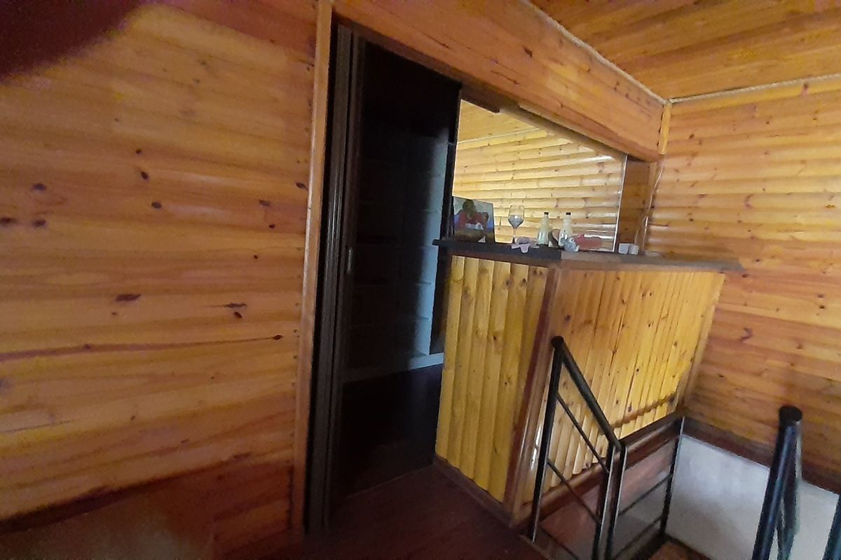 Interior view of a rustic living area featuring extensive timber wall and ceiling cladding, a built-in bar counter, and staircase access.