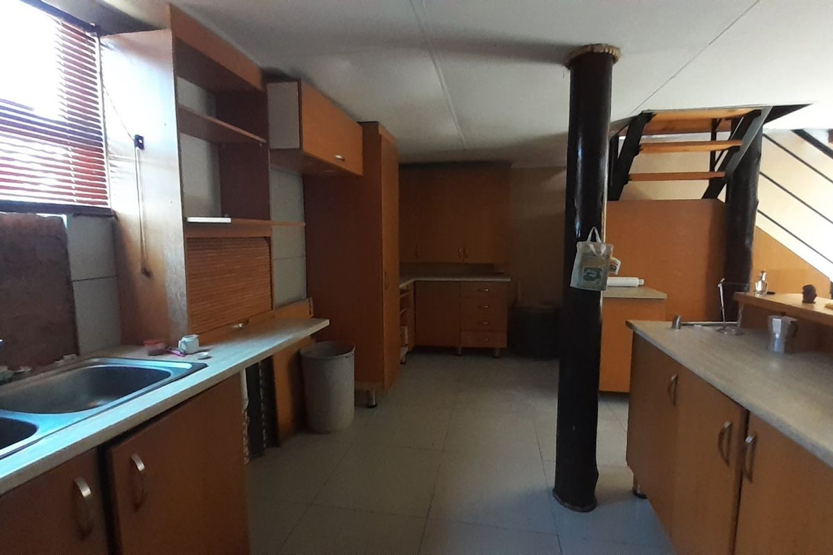 A dated kitchen featuring extensive built-in cabinetry, laminate countertops, and a double bowl sink, with an integrated staircase leading to an upper level.