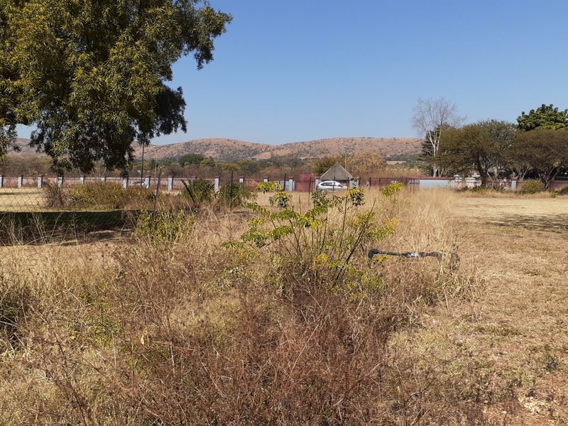 A wide-angle view of a large, undeveloped farm plot featuring dry grass, perimeter fencing, and mature trees with distant mountain views.