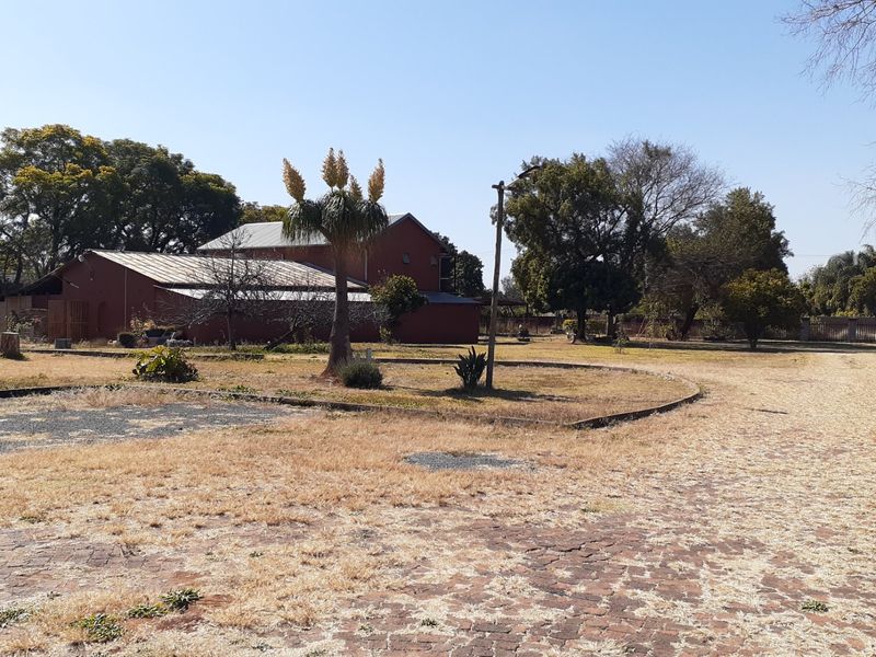 A wide view of the farm property grounds featuring a brick paved driveway, mature trees, and a water tank tower in a rural setting.