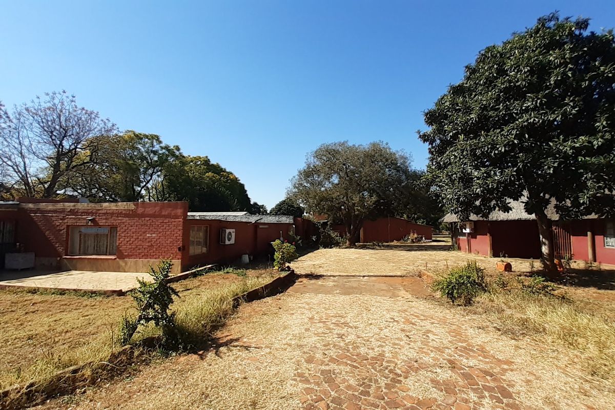 Rear view of the farm property featuring brick buildings, a paved driveway, and mature trees under a clear sky.