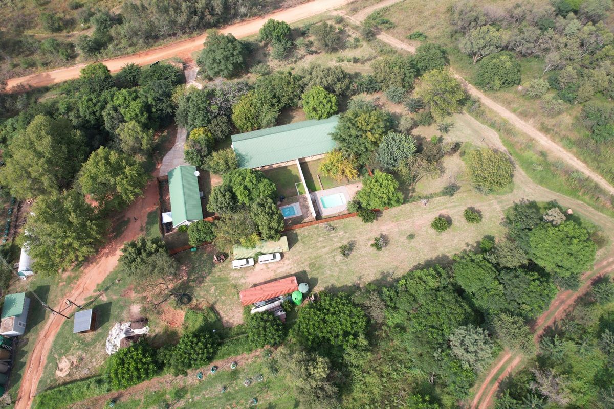 Aerial view of a farm property featuring multiple buildings, a swimming pool, and extensive surrounding land with mature trees and dirt access roads.
