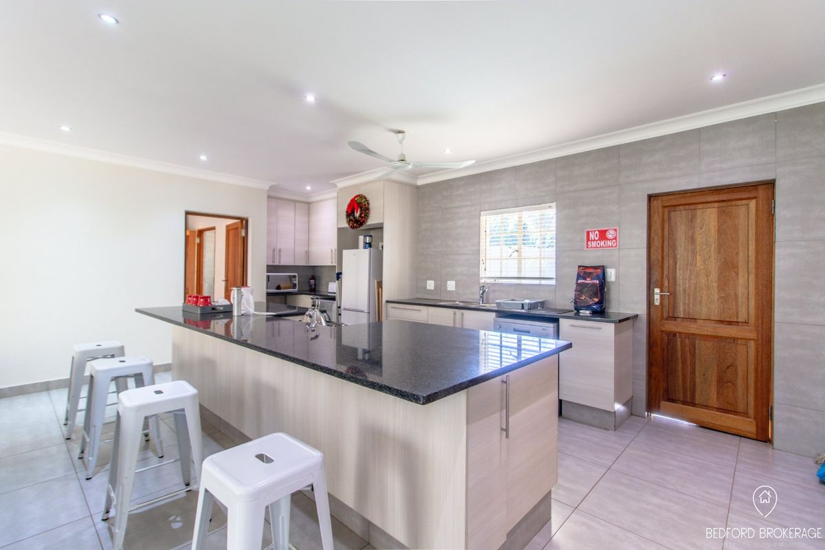 Modern kitchen featuring a large granite-topped island, neutral cabinetry, tiled backsplash, and recessed lighting, providing a functional and contemporary cooking and dining space.