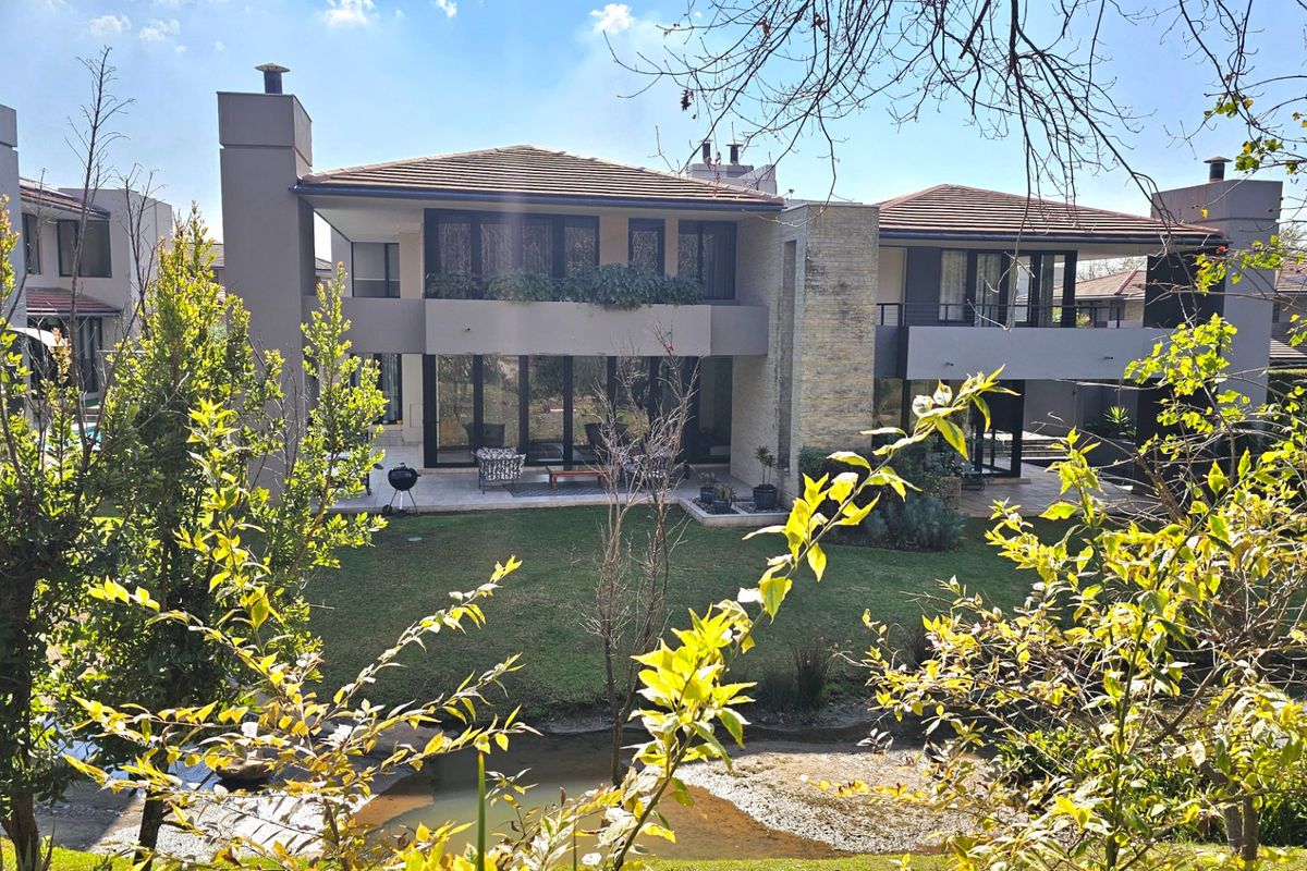 Rear view of a modern multi-story house featuring stone cladding, a covered patio, upper-level balconies, and large glass doors overlooking a landscaped garden.