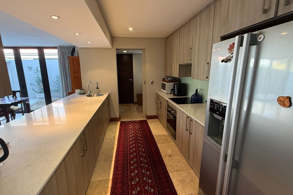 Modern kitchen featuring stone countertops, ample built-in cabinetry, integrated appliances, and stone flooring, with a seamless flow to the adjacent living area.