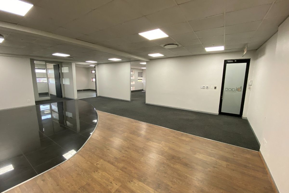 Spacious open-plan commercial office area featuring a mix of laminate, tile, and carpet flooring with modern recessed ceiling lighting and glass partition doors.