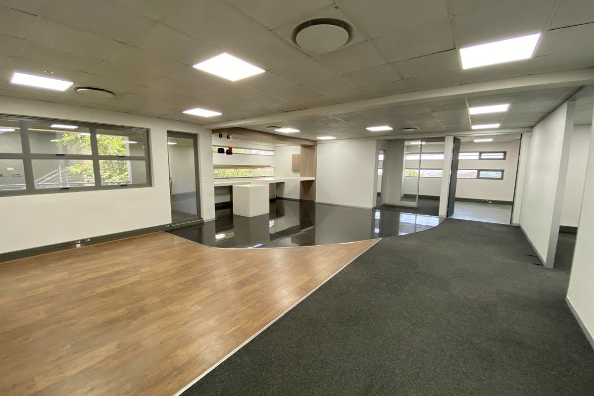 Spacious open-plan commercial office area featuring a mix of laminate, carpet, and tiled flooring, built-in kitchenette, and modern recessed ceiling lighting.