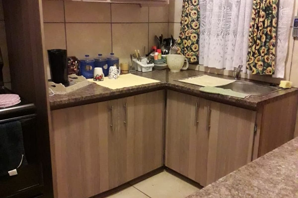 A functional kitchen featuring laminate cabinetry, durable countertops, a stainless steel sink, and tiled flooring, offering a practical layout for daily use.