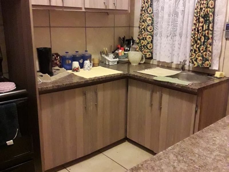 A functional kitchen featuring laminate cabinetry, durable countertops, a stainless steel sink, and tiled flooring, offering a practical layout for daily use.