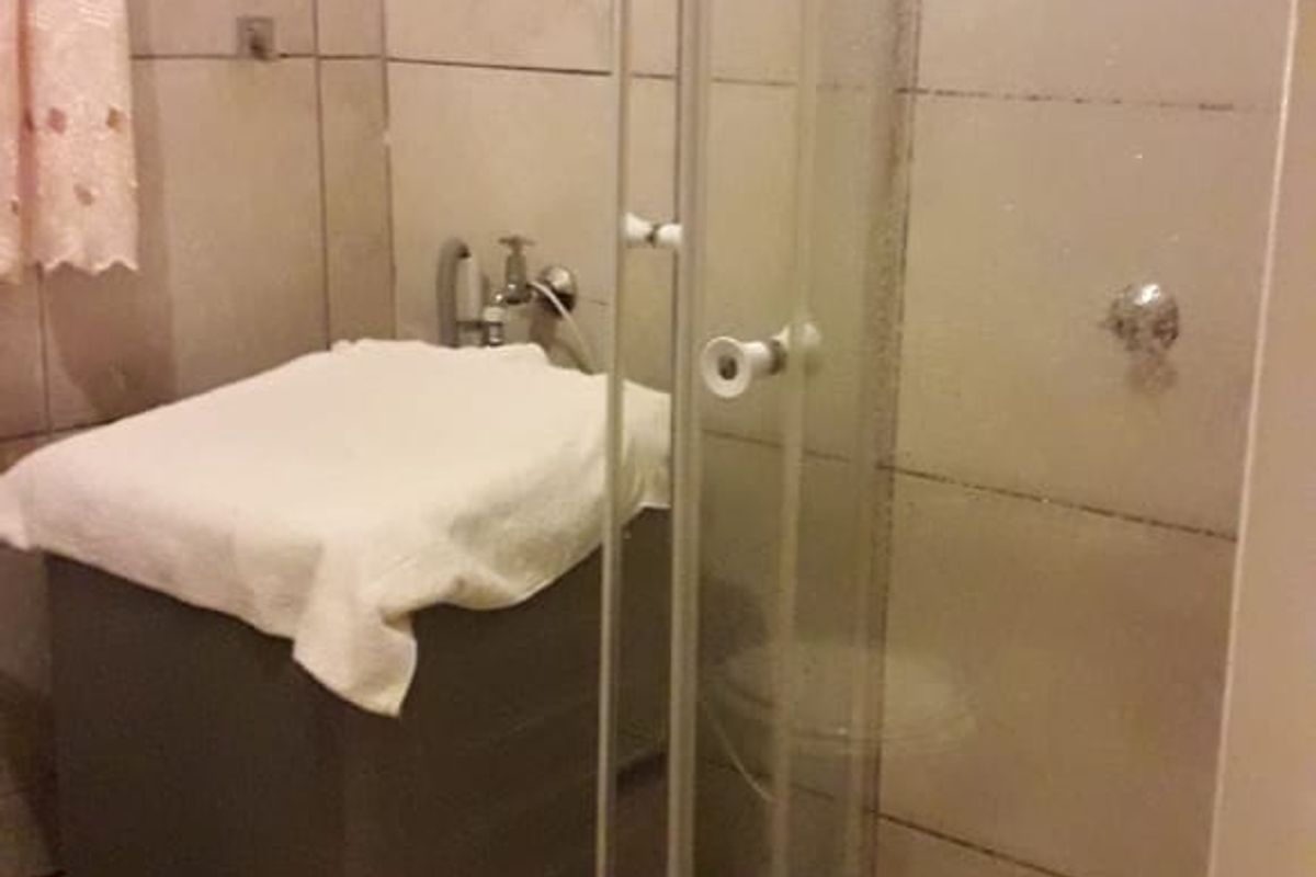A compact bathroom featuring a glass shower enclosure with tiled walls and flooring, requiring some maintenance and updates to the fixtures.