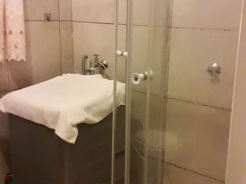 A compact bathroom featuring a glass shower enclosure with tiled walls and flooring, requiring some maintenance and updates to the fixtures.