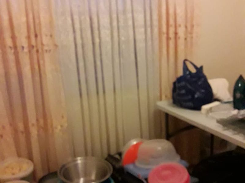 A cluttered interior space featuring a window with curtains, currently used for storage.