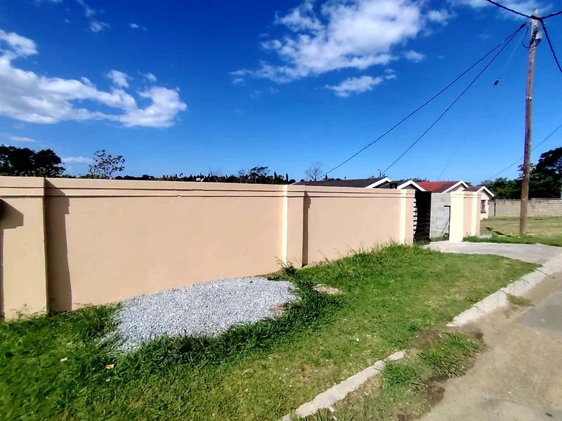 A view of the property's front perimeter wall and entrance area, featuring a concrete driveway and grass verge.