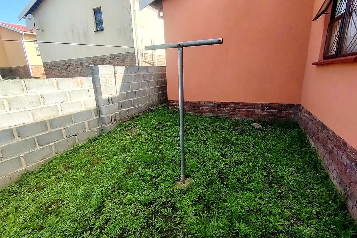 A rear exterior area featuring a small grassed yard, a metal washing line, and concrete block boundary walls.