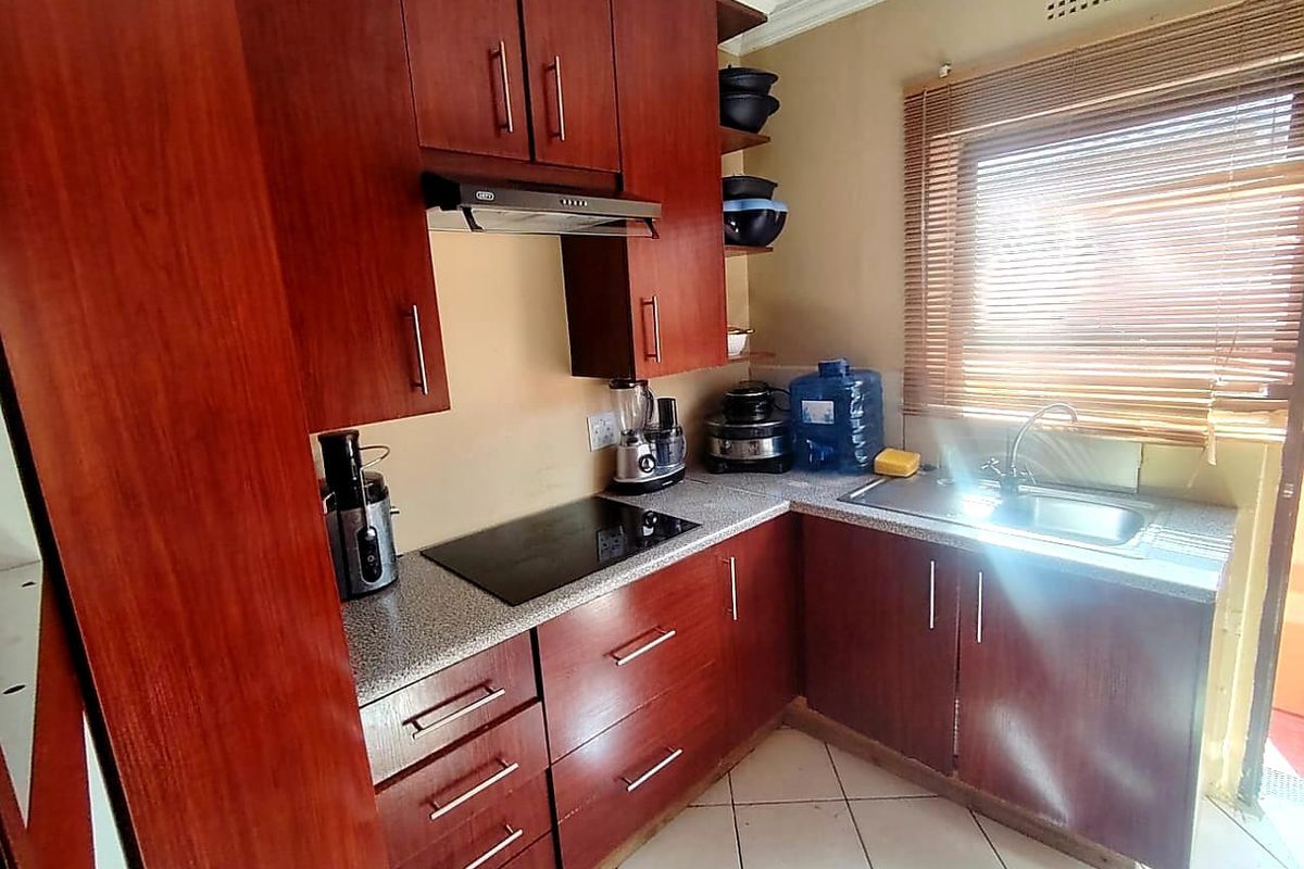 Compact kitchen featuring dark wood-look cabinetry, granite countertops, an integrated electric hob with extractor fan, and a stainless steel sink.