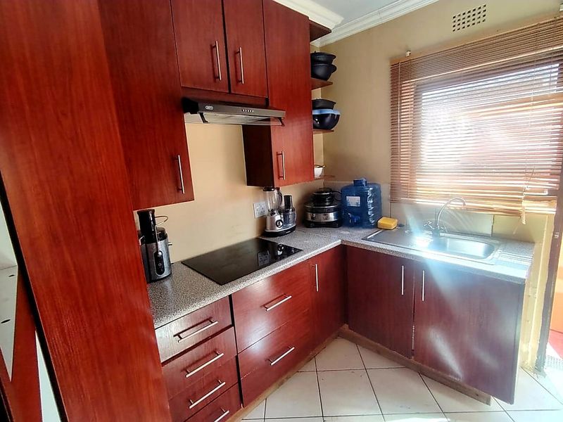Compact kitchen featuring dark wood-look cabinetry, granite countertops, an integrated electric hob with extractor fan, and a stainless steel sink.