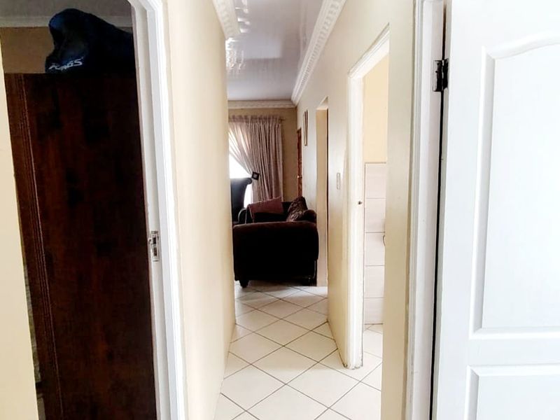 A bright, tiled hallway featuring decorative ceiling cornicing and access to multiple rooms, providing a clean and functional transition space.