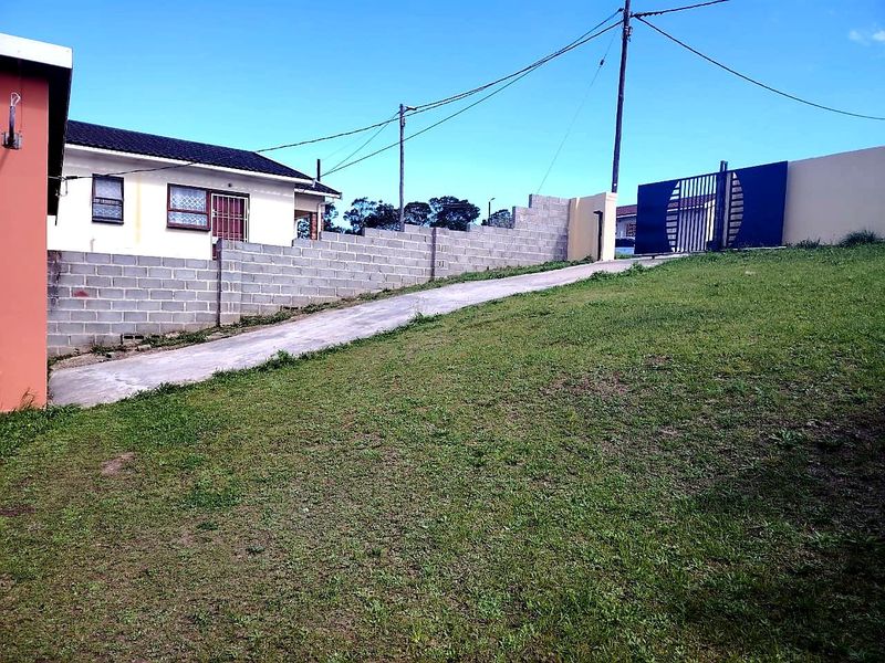Front view of the property featuring a concrete driveway, metal entrance gate, and an unfinished concrete block boundary wall on a sloped lawn.