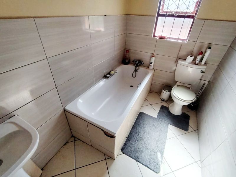 A compact bathroom featuring a standard bathtub, pedestal basin, and toilet with neutral ceramic wall and floor tiling.