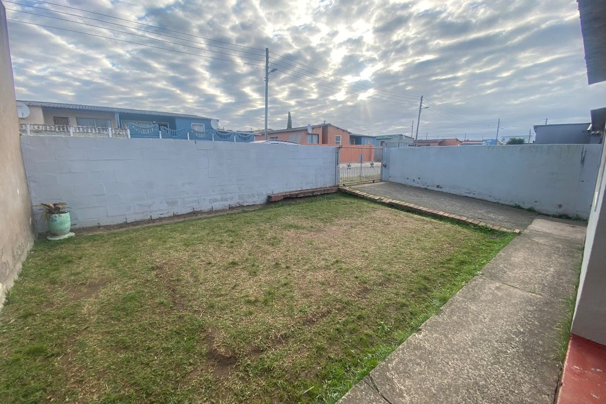 A private rear yard featuring a concrete block boundary wall, paved driveway area, and a small lawn space.
