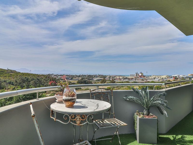 A spacious balcony featuring artificial grass flooring, a metal balustrade, and expansive panoramic views of the surrounding landscape and distant coastline.