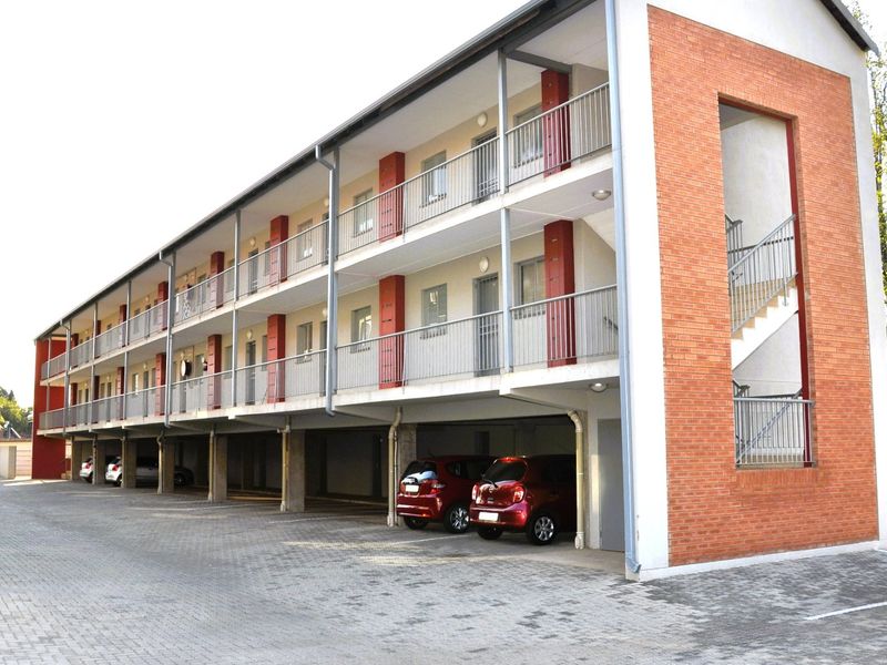 A multi-story apartment building featuring a brick facade, open-air balconies with metal railings, and ground-level covered parking.