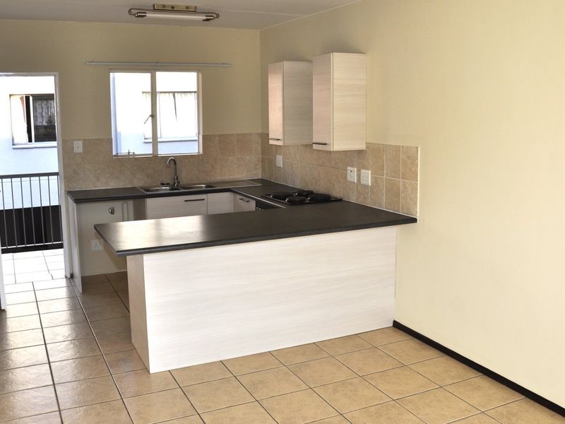 An open-plan kitchen area featuring light wood-finish cabinetry, dark laminate countertops, ceramic tile backsplash, and tiled flooring, leading to an exterior balcony.