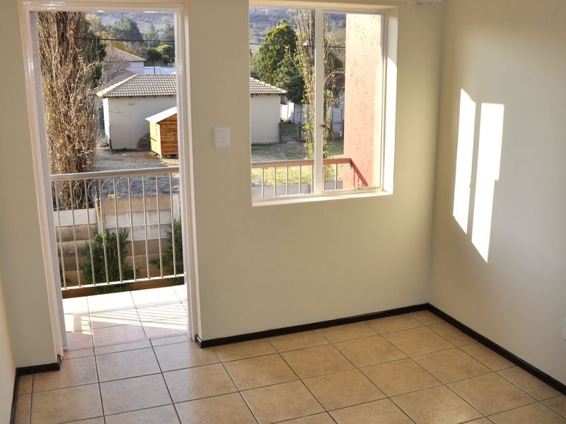 A bright, empty bedroom featuring tiled flooring, neutral walls, and direct access to a private balcony through a glass door.