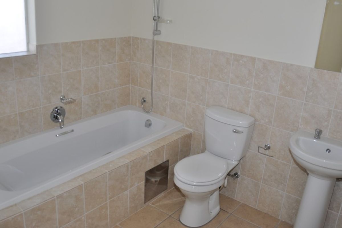 A functional bathroom featuring a bathtub with shower mixer, pedestal basin, and toilet, finished with neutral wall and floor tiling.