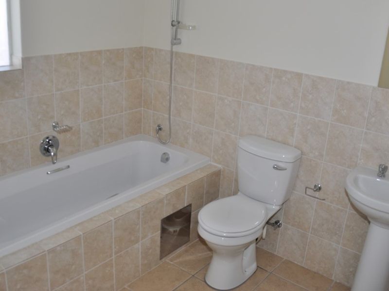 A functional bathroom featuring a bathtub with shower mixer, pedestal basin, and toilet, finished with neutral wall and floor tiling.
