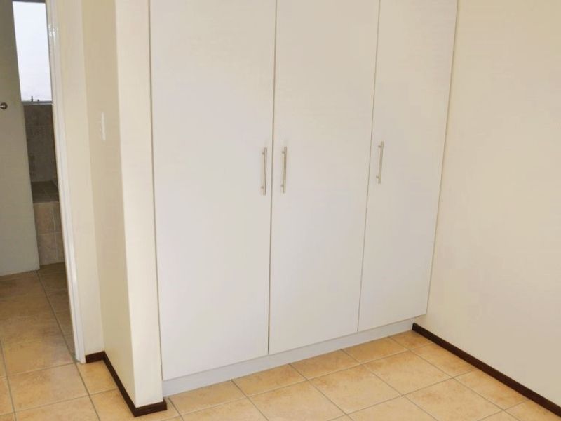 A clean, empty bedroom featuring neutral tiled flooring and ample built-in cupboard storage, with direct access to an adjoining bathroom.