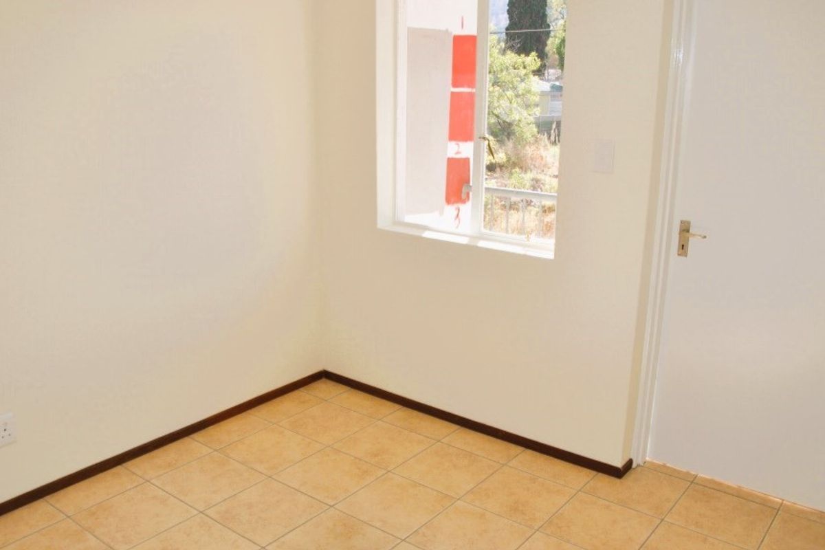 A clean, empty bedroom featuring neutral walls, tiled flooring, and a window providing natural light.