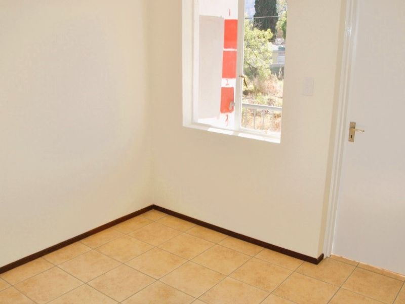A clean, empty bedroom featuring neutral walls, tiled flooring, and a window providing natural light.