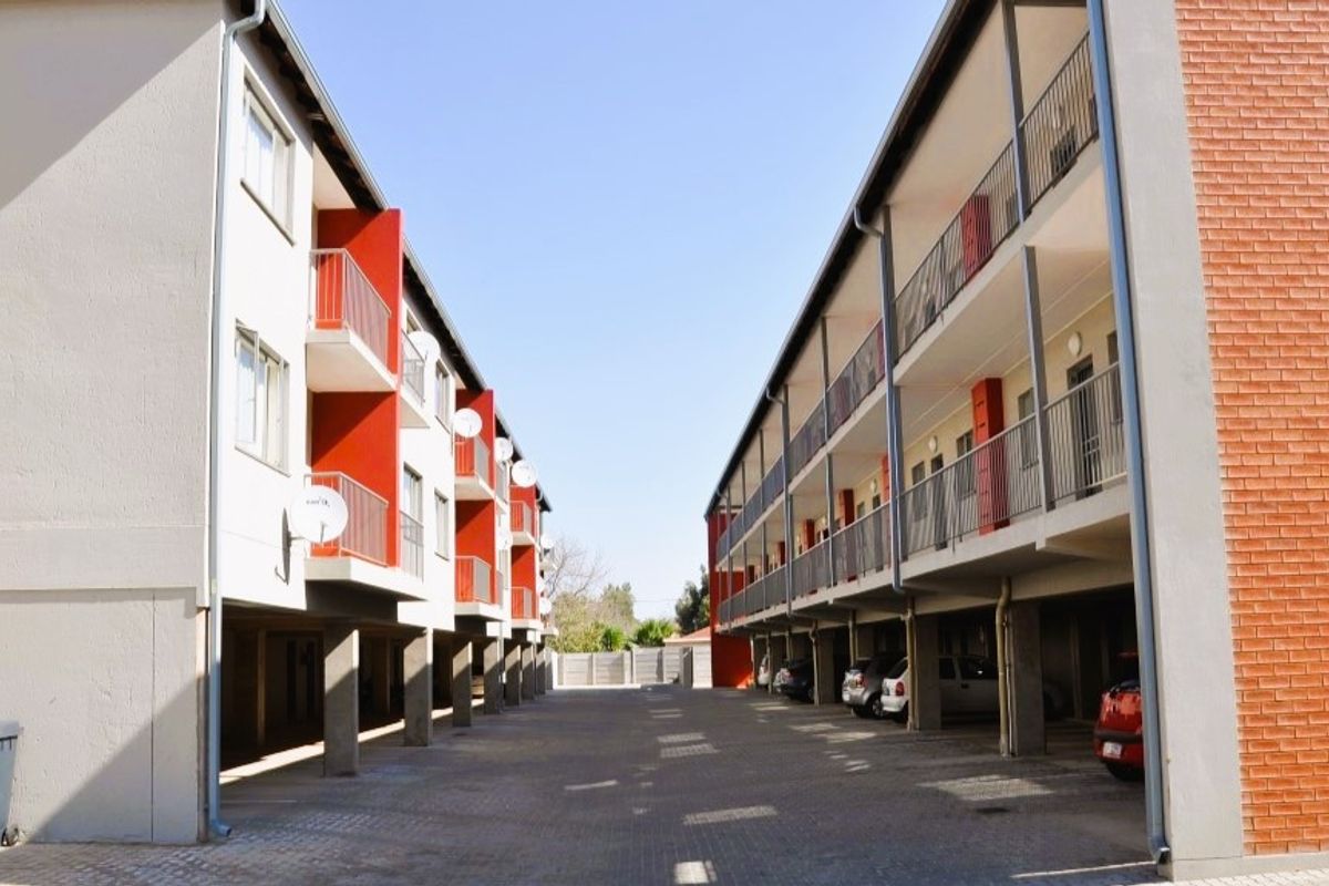 Exterior view of an apartment complex featuring paved parking areas, multi-level balconies, and a combination of brick and painted concrete facade finishes.