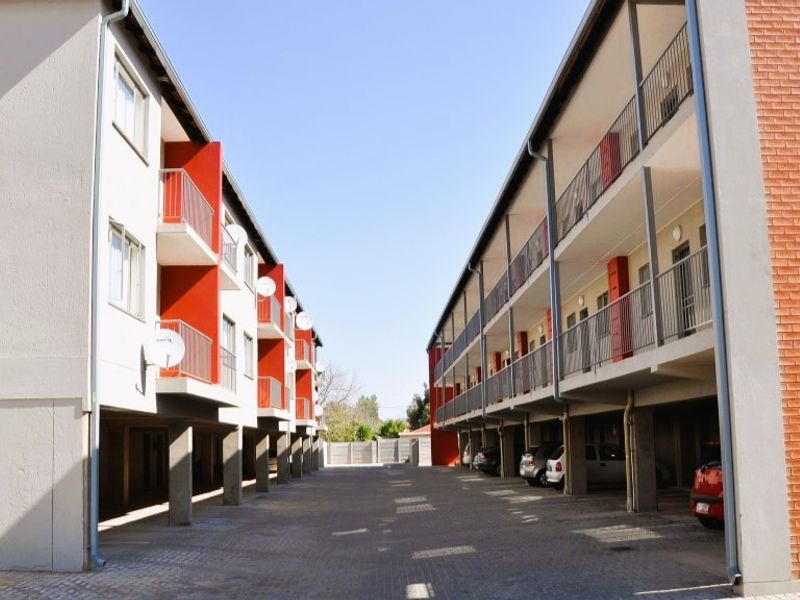 Exterior view of an apartment complex featuring paved parking areas, multi-level balconies, and a combination of brick and painted concrete facade finishes.