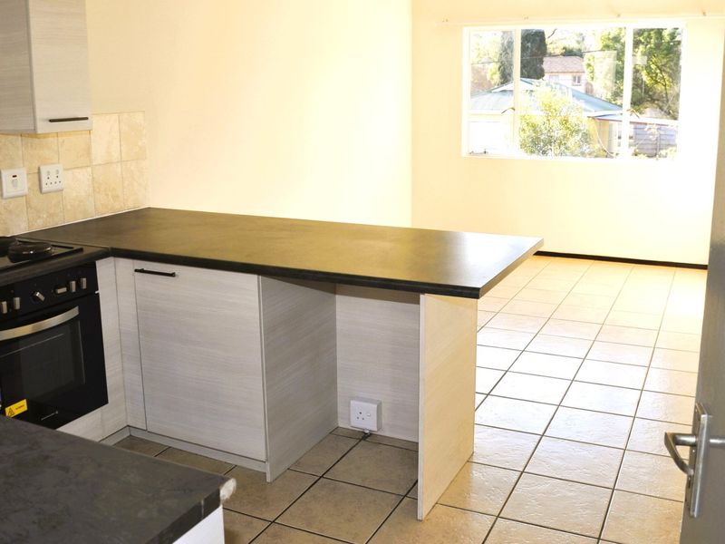 An open-plan kitchen and living area featuring tiled floors, modern laminate cabinetry, and built-in cooking appliances, offering a bright and functional space.