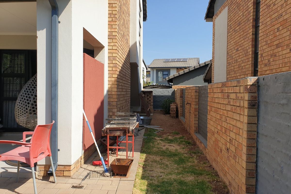 A side yard area featuring a paved walkway, brick boundary wall, and access to a covered patio space.