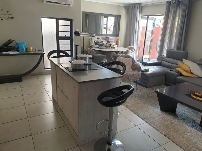 Open-plan living area featuring a central kitchen island with a built-in hob, tiled flooring, and sliding glass doors leading to the outdoor space.