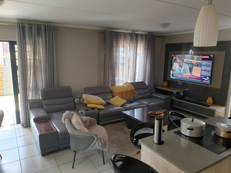 Spacious open-plan living area featuring tiled floors, a modern built-in media wall, and seamless access to the outdoor space through sliding glass doors.