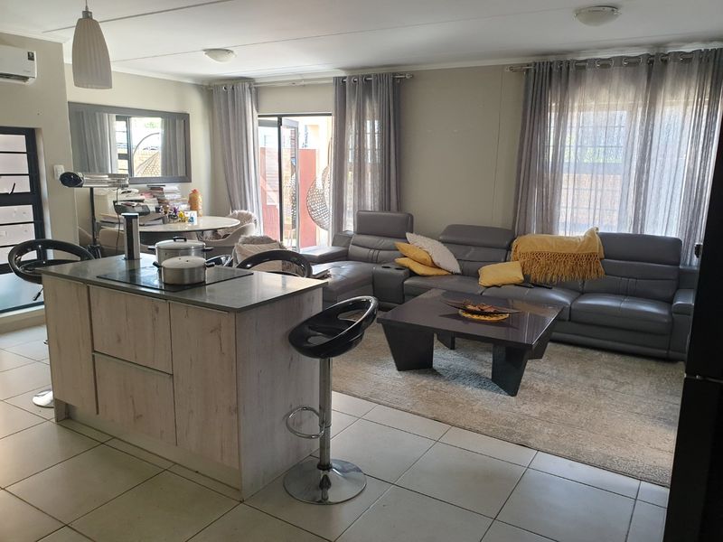 An open-plan living area featuring a modern kitchen island with a built-in hob, tiled flooring, and sliding glass doors leading to the exterior.