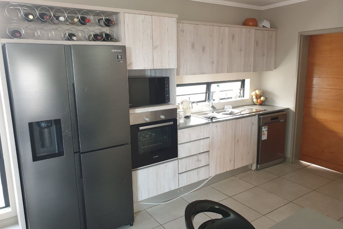 Modern kitchen featuring light wood-grain cabinetry, built-in oven, microwave, stainless steel sink, and tiled flooring with ample storage space.