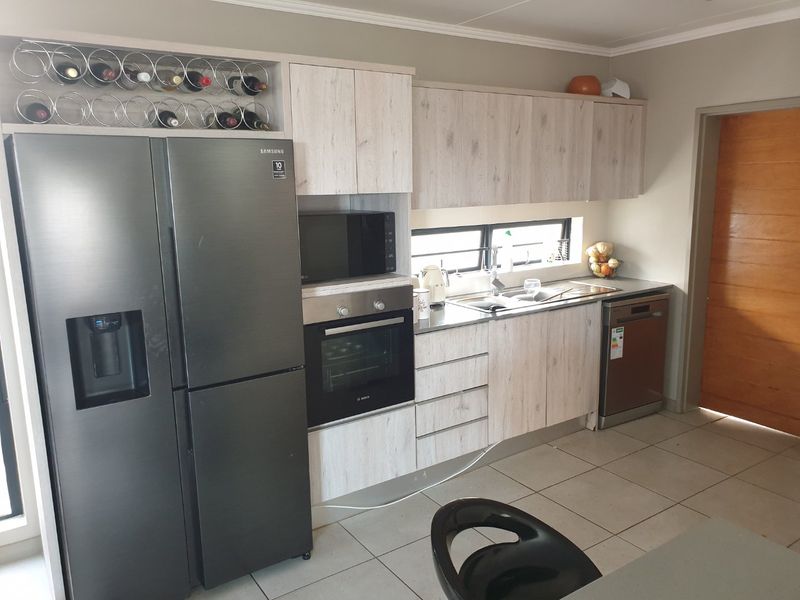 Modern kitchen featuring light wood-grain cabinetry, built-in oven, microwave, stainless steel sink, and tiled flooring with ample storage space.