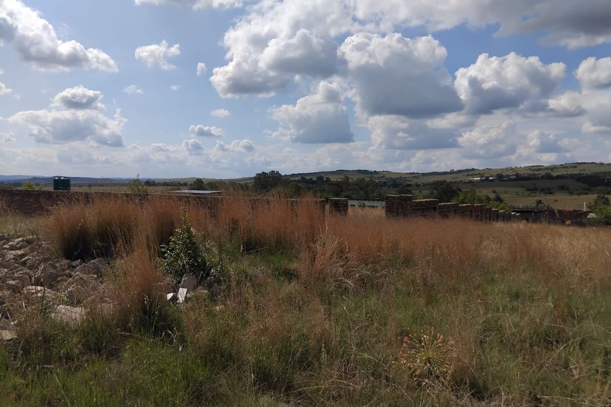 A view of the vacant residential land featuring a brick boundary wall and expansive landscape under a cloudy sky.