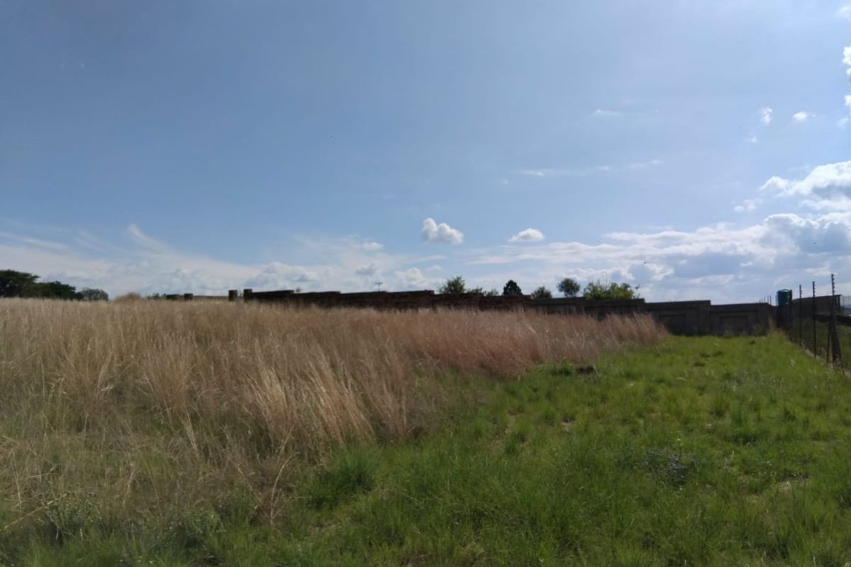 A view of a vacant residential plot featuring tall grass, a perimeter boundary wall, and installed electric fencing.