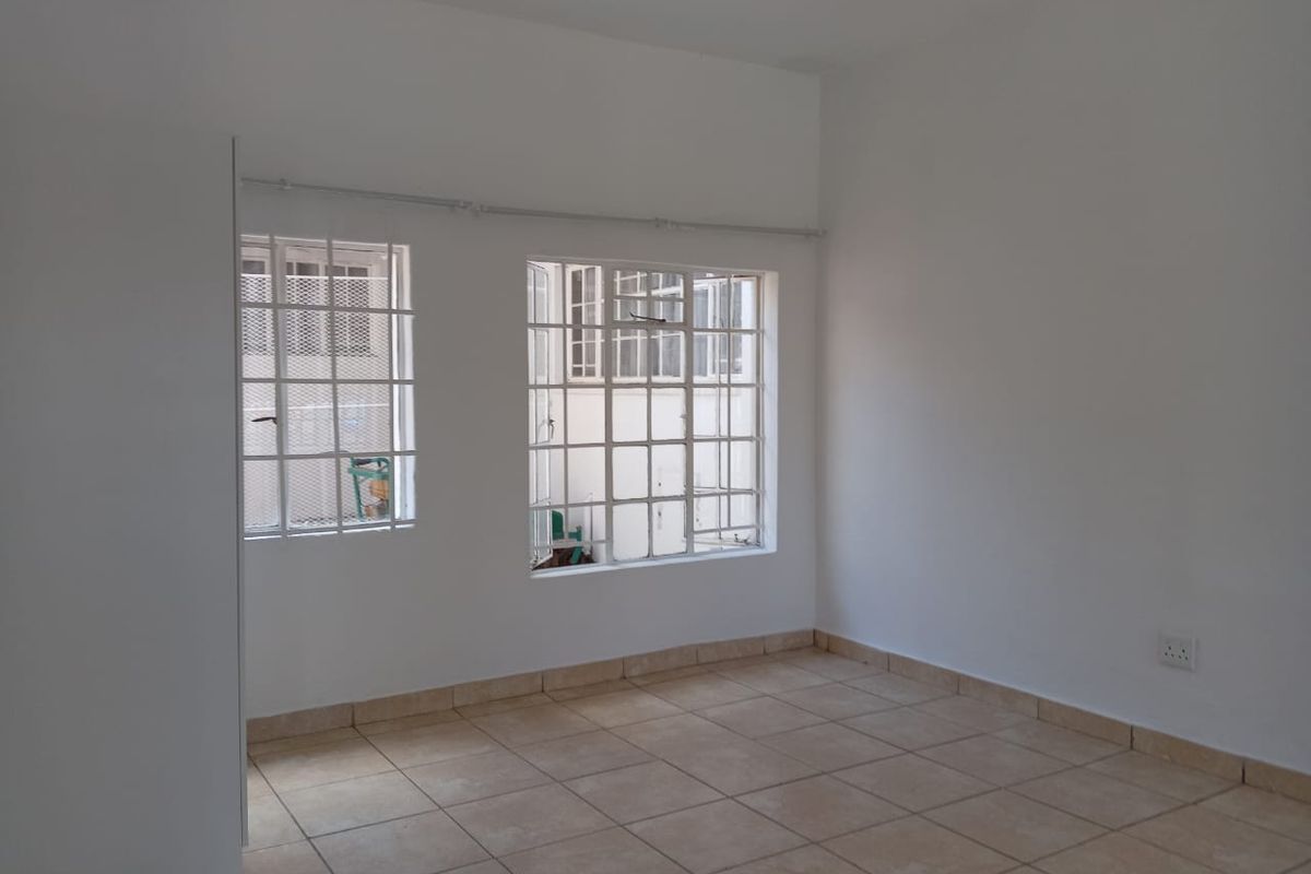 A bright, empty bedroom featuring tiled flooring, built-in cupboard storage, and windows fitted with security bars.